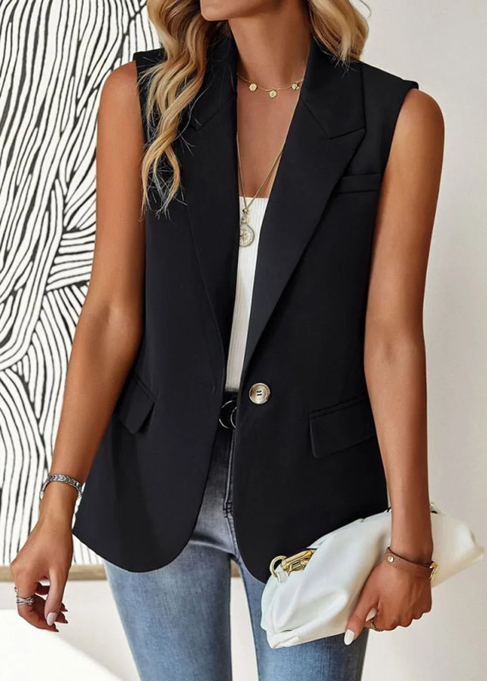 Sleek black sleeveless blazer with a single button closure, worn by a model with light blue jeans and a white clutch.
