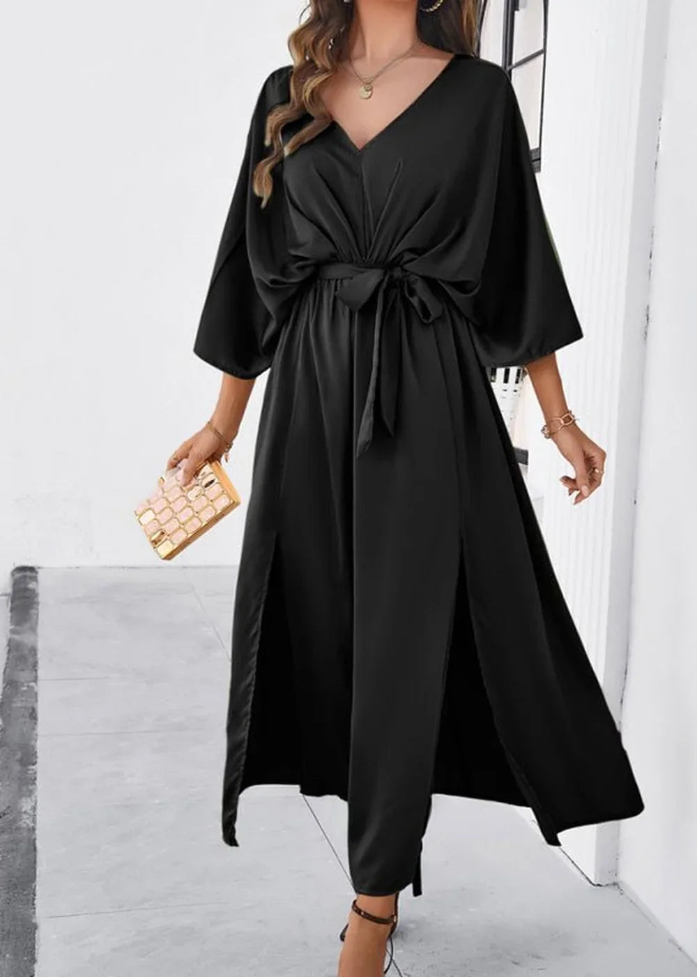 Black satin V-neck maxi dress with wide sleeves, a tie waist, and thigh-high slits, held by a model.