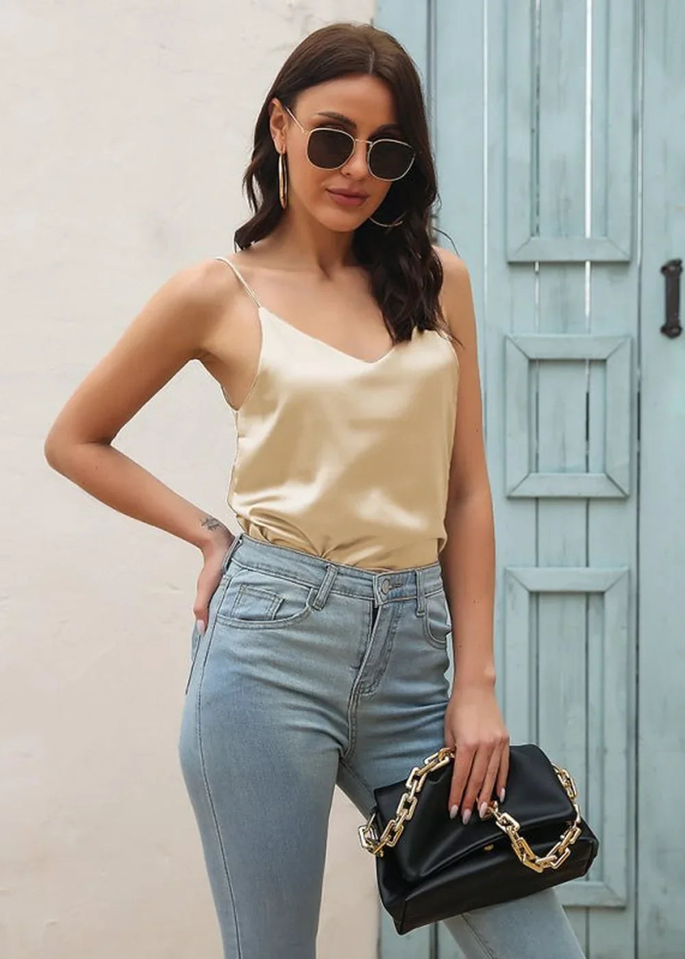 Satin champagne camisole with spaghetti straps worn with light wash jeans and a black clutch.