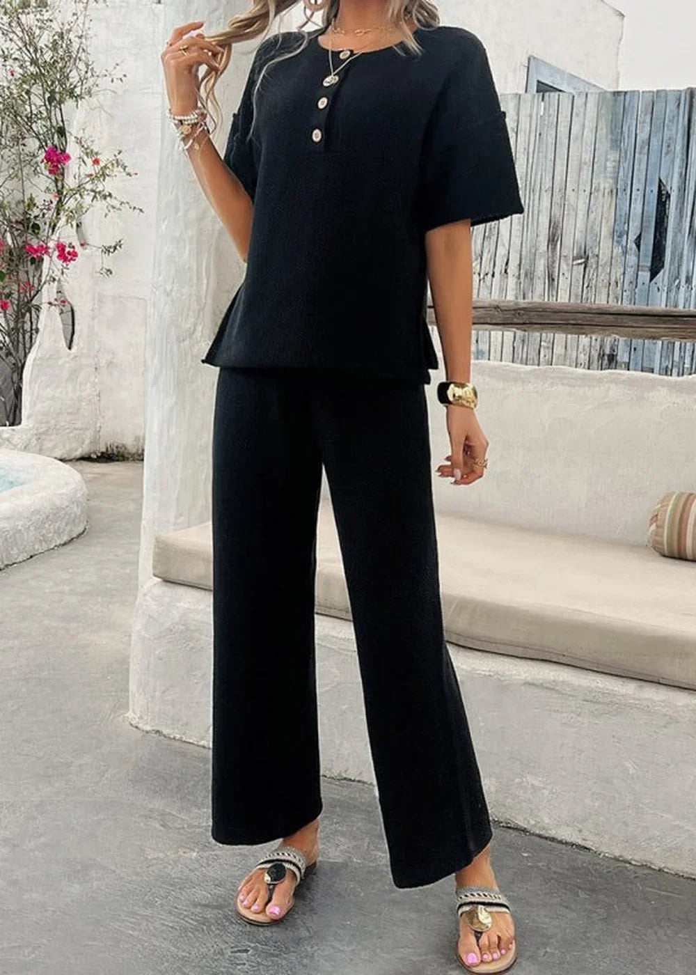 Black short-sleeve top and wide-leg pants set with button detail and gold bracelet.