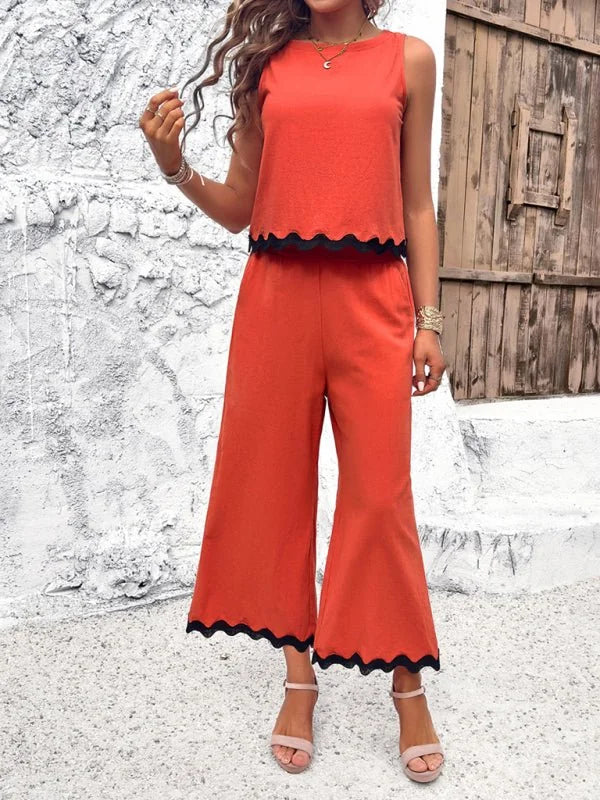 Orange wide-leg cropped pantsuit with scalloped black trim, worn by a model with pink heels.