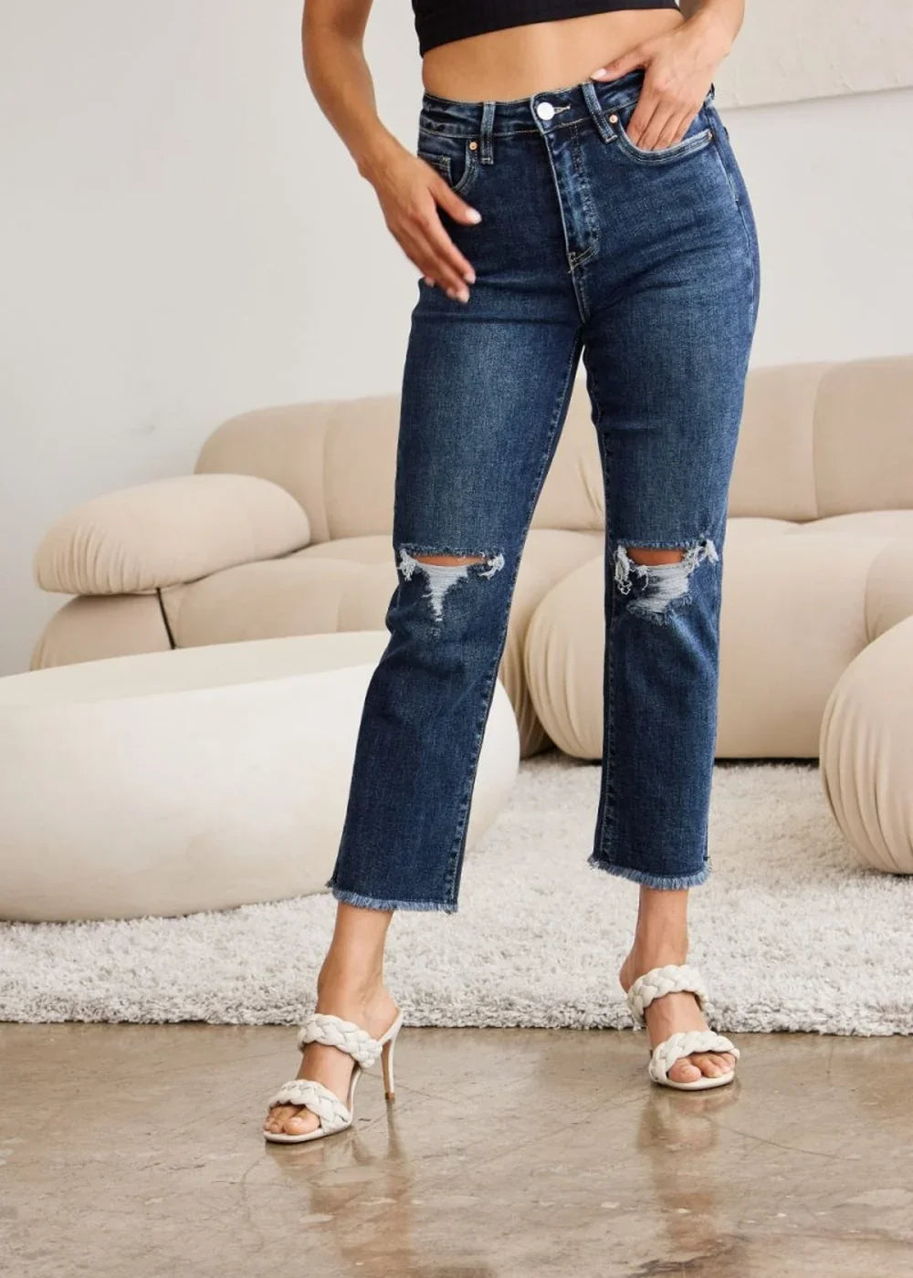 Distressed dark wash denim jeans with frayed hems and ripped knees on a model.