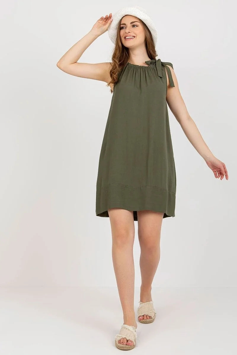 Olive green sleeveless loose-fit dress with tie shoulders and straw hat on model.