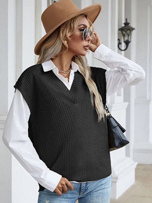 Woman in a black v-neck knit vest over a white collared shirt, wearing a tan hat and blue jeans.