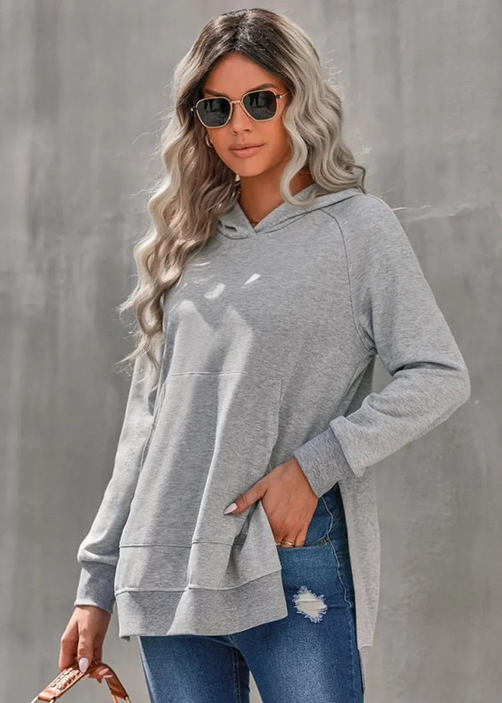 Gray hooded tunic sweatshirt with side slits, worn by a model with blonde wavy hair and sunglasses.