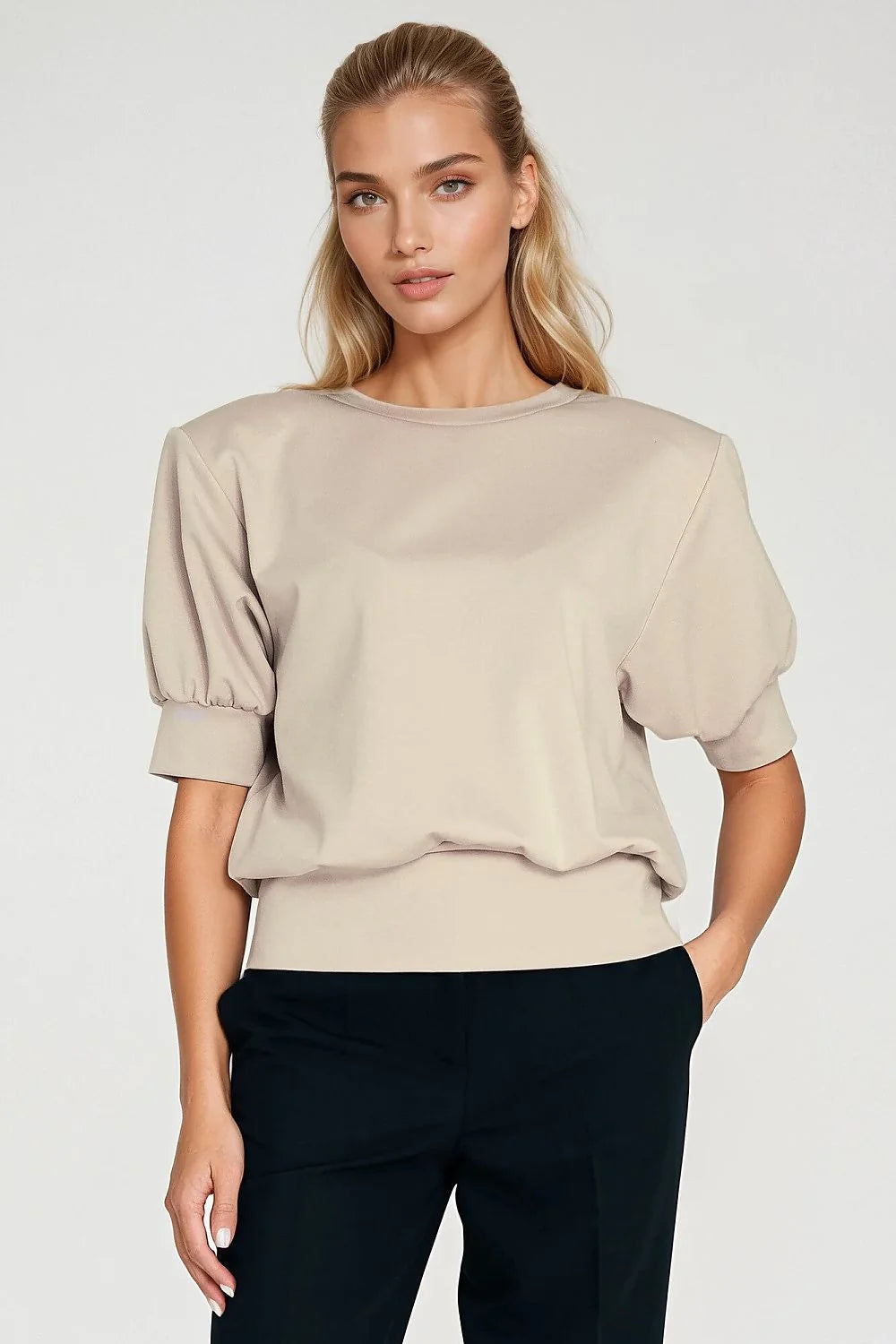 Model in oversized beige top with cinched waist and puffed sleeves, and black pants.