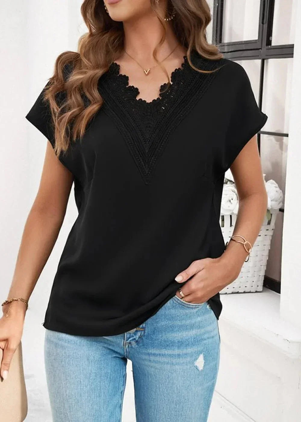 Black V-neck top with lace trim and short sleeves, paired with light wash distressed denim jeans.