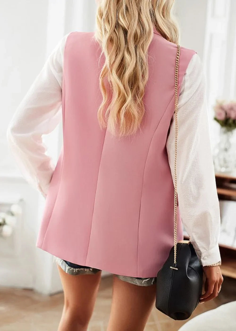 Back view of a pink blazer over a white shirt, with a black purse with a gold chain strap.