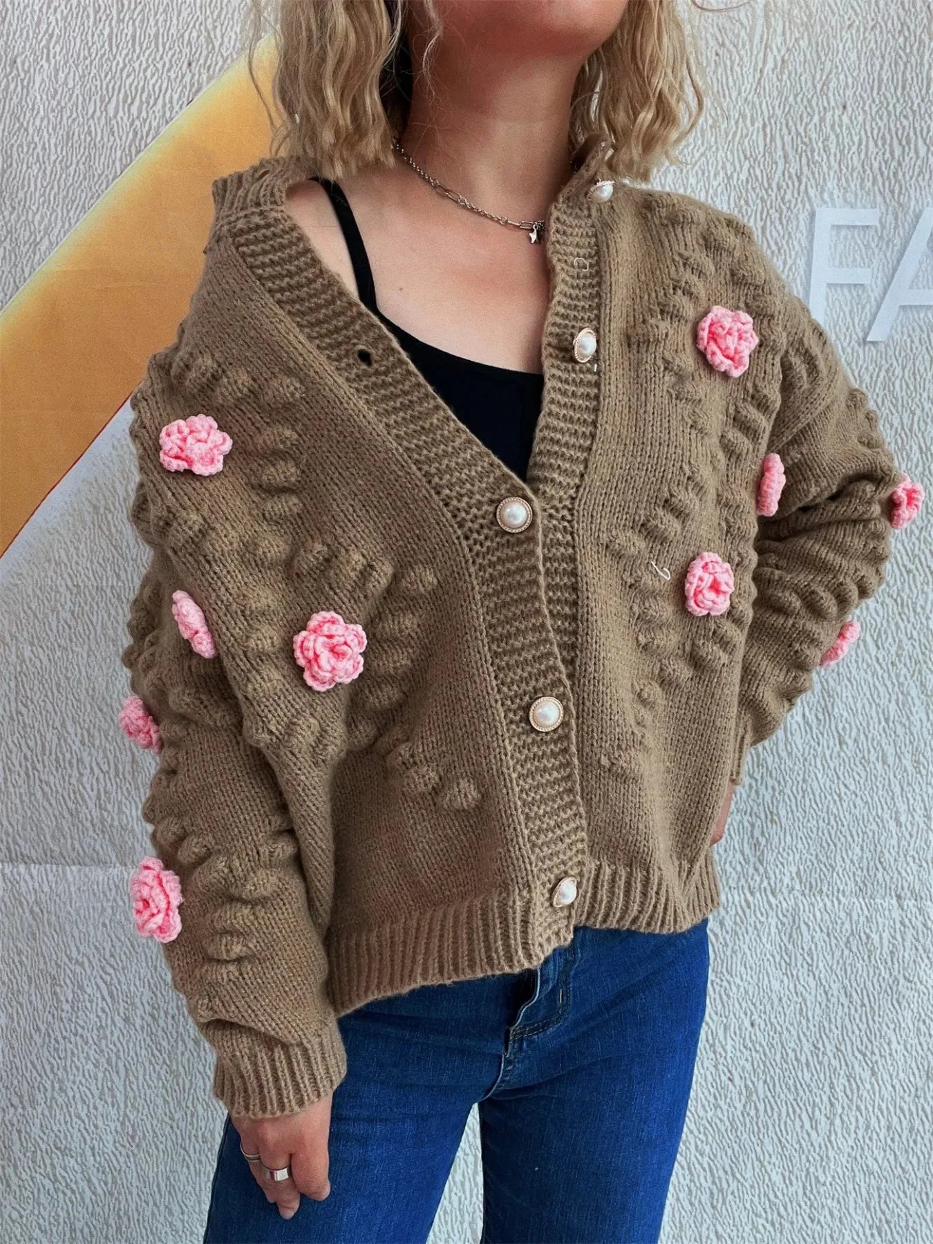 Brown knit cardigan with pink floral appliques and pearl buttons, on a model.