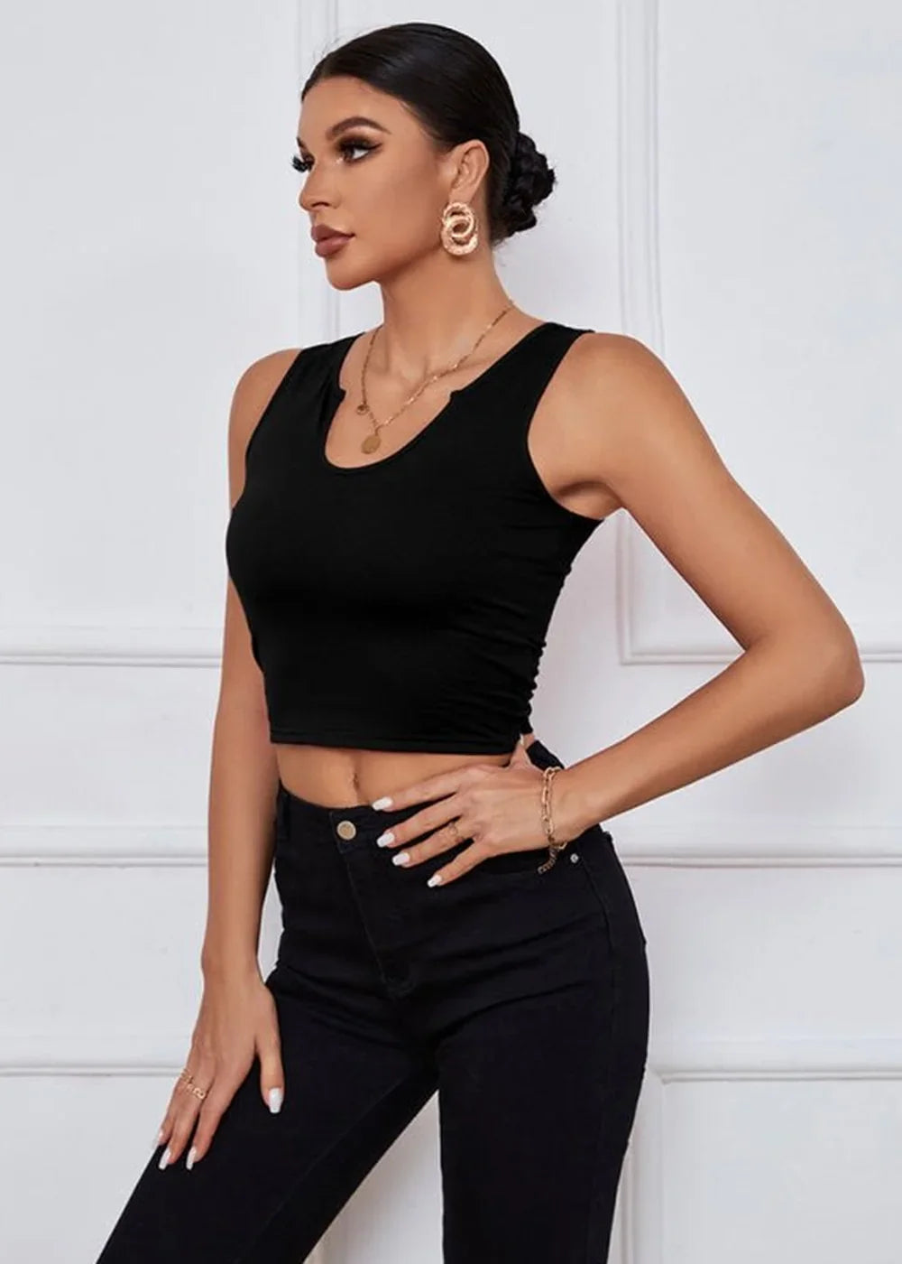 Woman in a black sleeveless crop top and black jeans, gold necklace and earrings