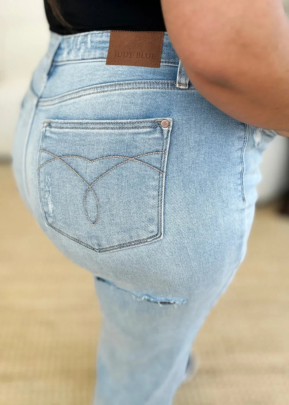 Close-up of light wash distressed denim jeans with brown leather patch and stitching detail.