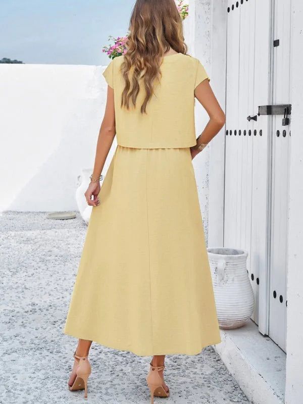 Back view of a woman wearing a yellow two-piece outfit with a cropped top and a flowing midi skirt.