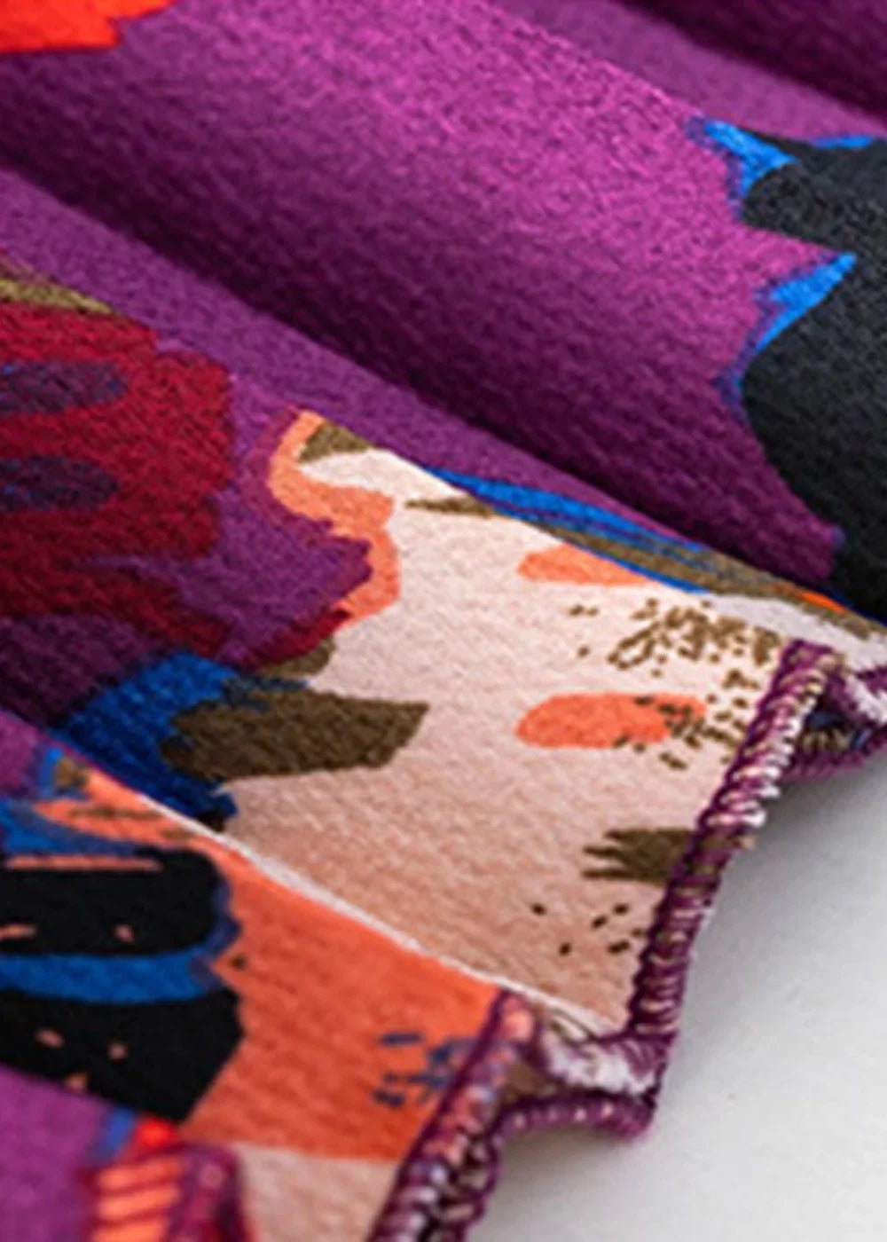 Close-up of purple fabric with a vibrant floral print in red, orange, blue, and black, with a textured finish.