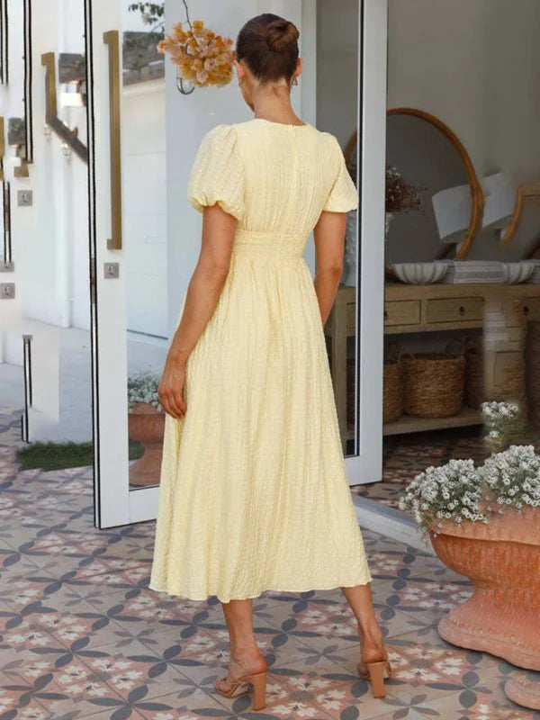 Light yellow textured midi dress with puff sleeves and a cinched waist, worn by a model from behind.