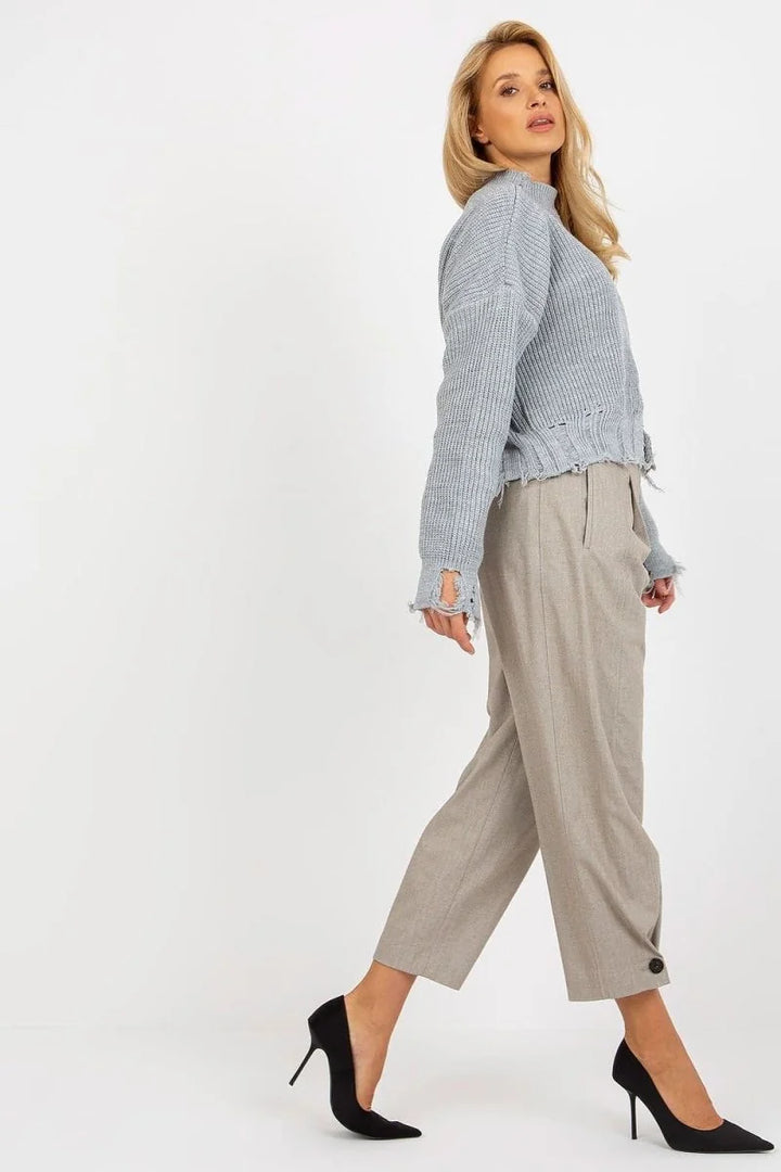 Light blue distressed knit sweater with frayed hem, worn with taupe trousers.