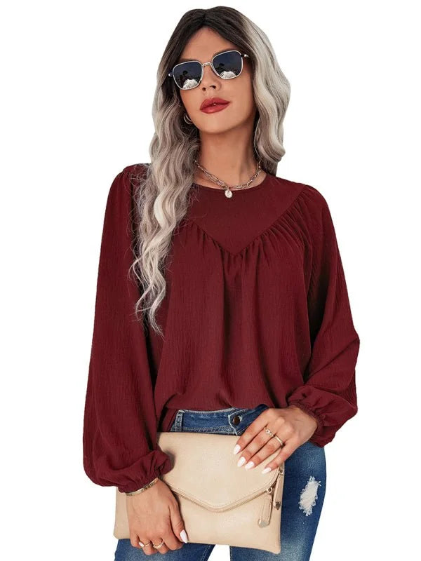Burgundy textured long-sleeve blouse with gathered neckline, worn by a model holding a cream clutch.
