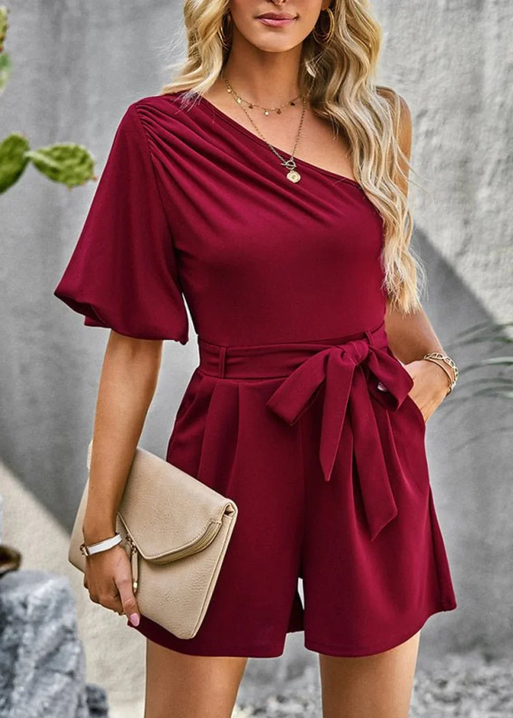 Maroon one-shoulder romper with ruched detail, belted waist, and short sleeves.