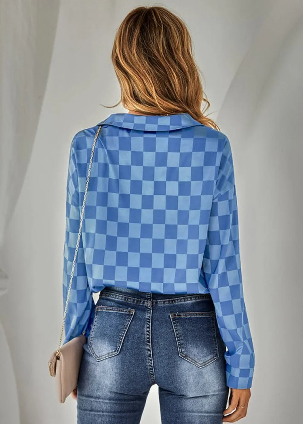 Back view of a woman wearing a blue and light blue checkered long-sleeve top and distressed denim jeans.