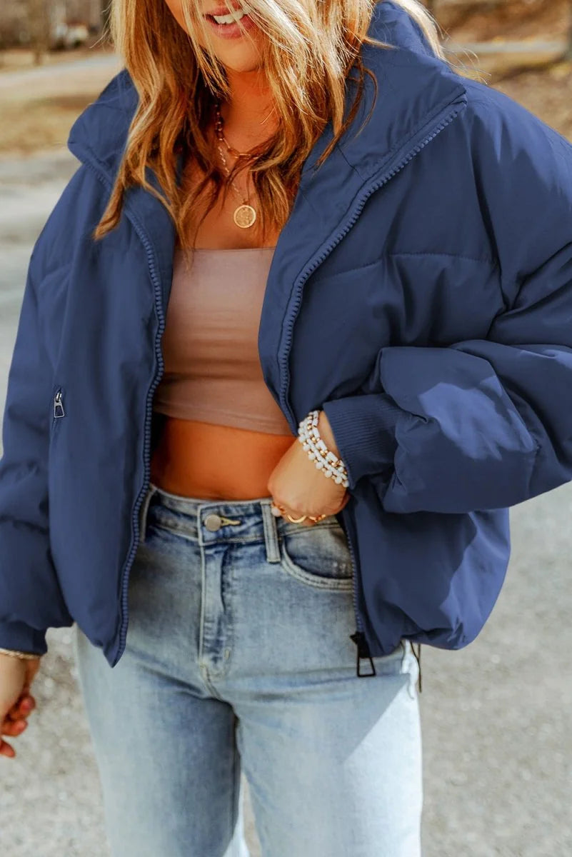 Navy blue puffer jacket with a standing collar and zipper, worn by a model with light wash jeans.