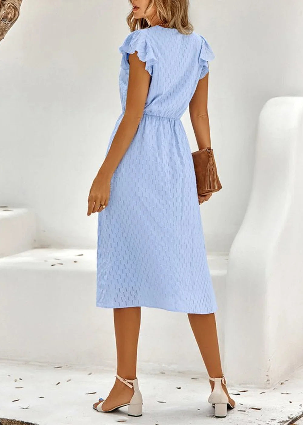 Light blue textured midi dress with flutter sleeves and a brown clutch.