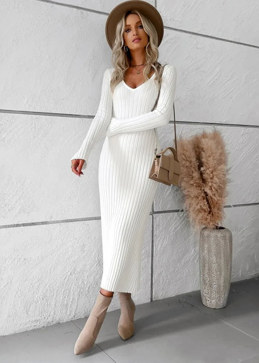 Woman in a white ribbed long-sleeve sweater dress, tan hat, and ankle boots, carrying a tan handbag.