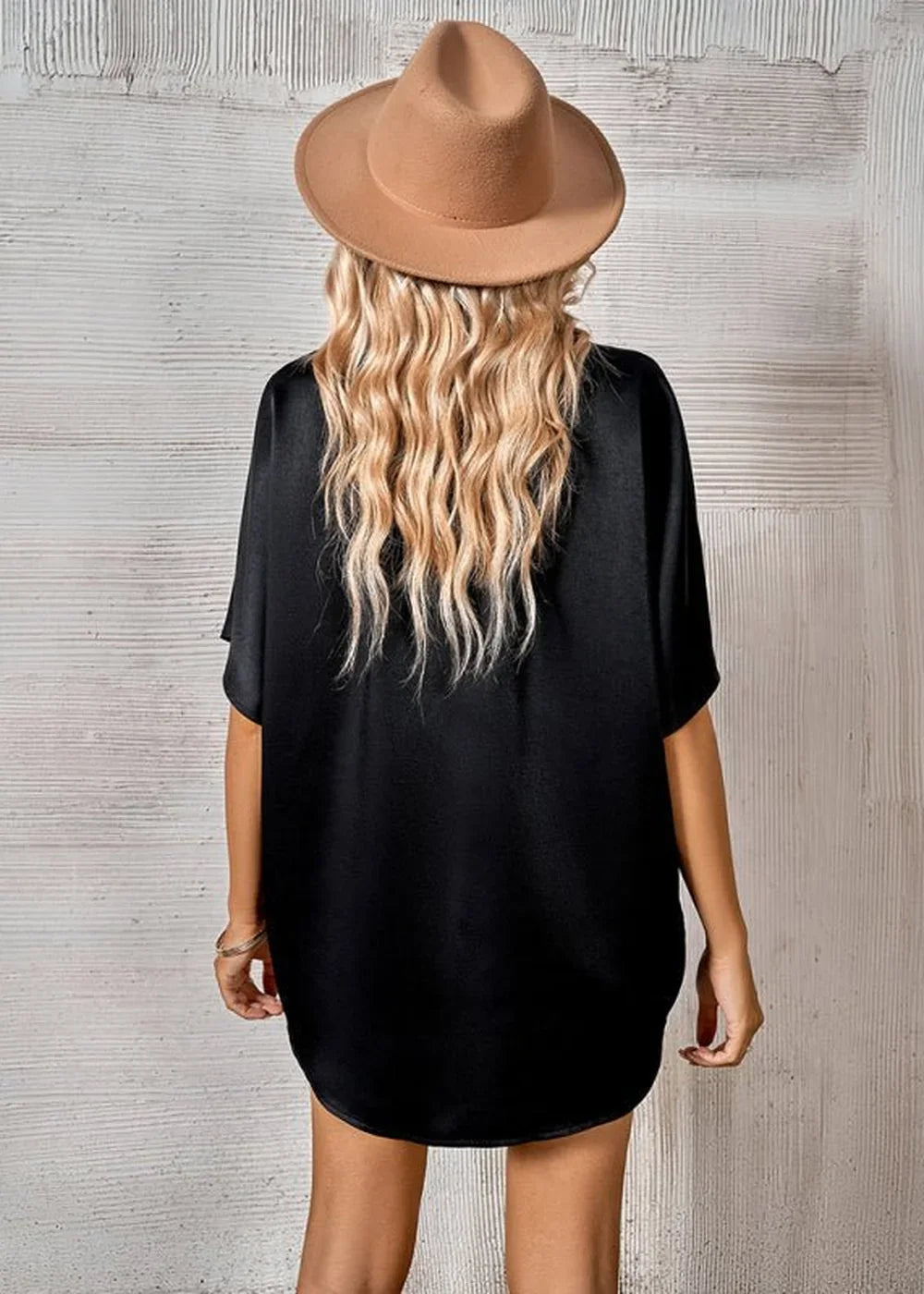 Woman from behind wearing a black t-shirt and a tan fedora hat with wavy blonde hair.