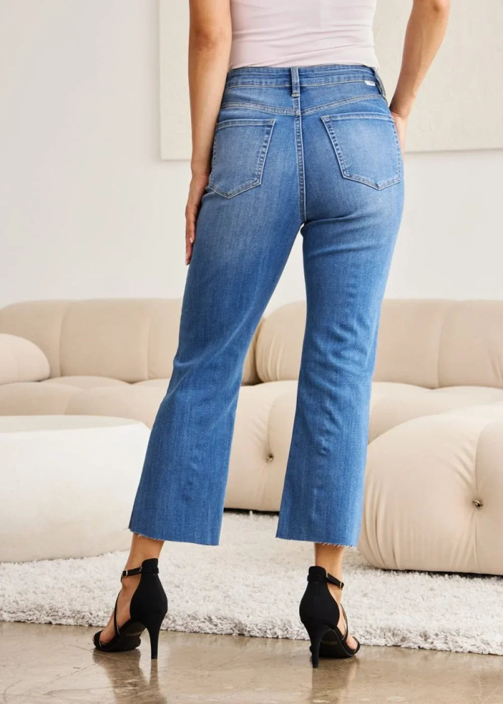 Blue denim jeans with frayed hem, showing back view on model.