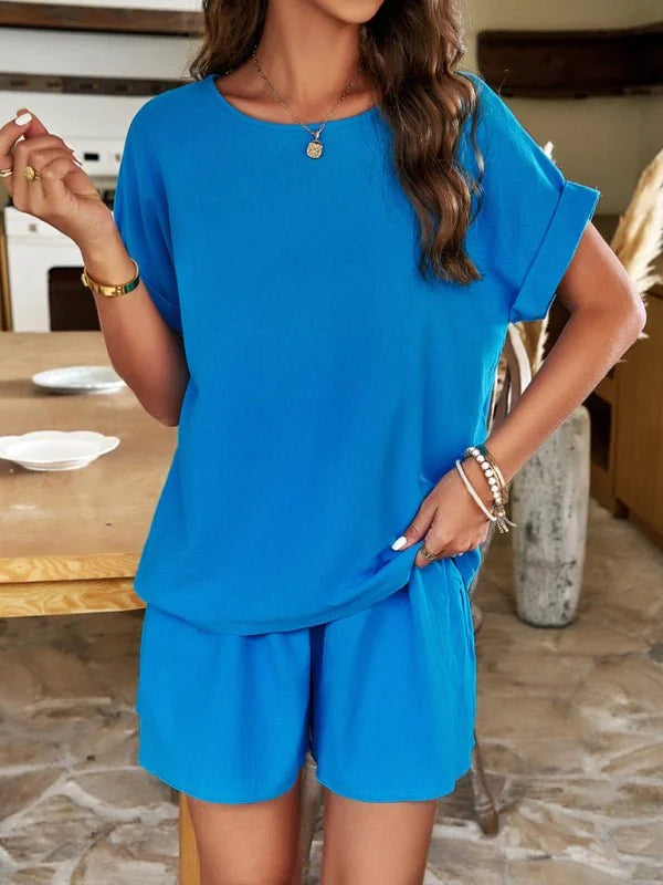 A woman models a bright blue polyester short suit with cuffed sleeves and elastic-waist shorts.