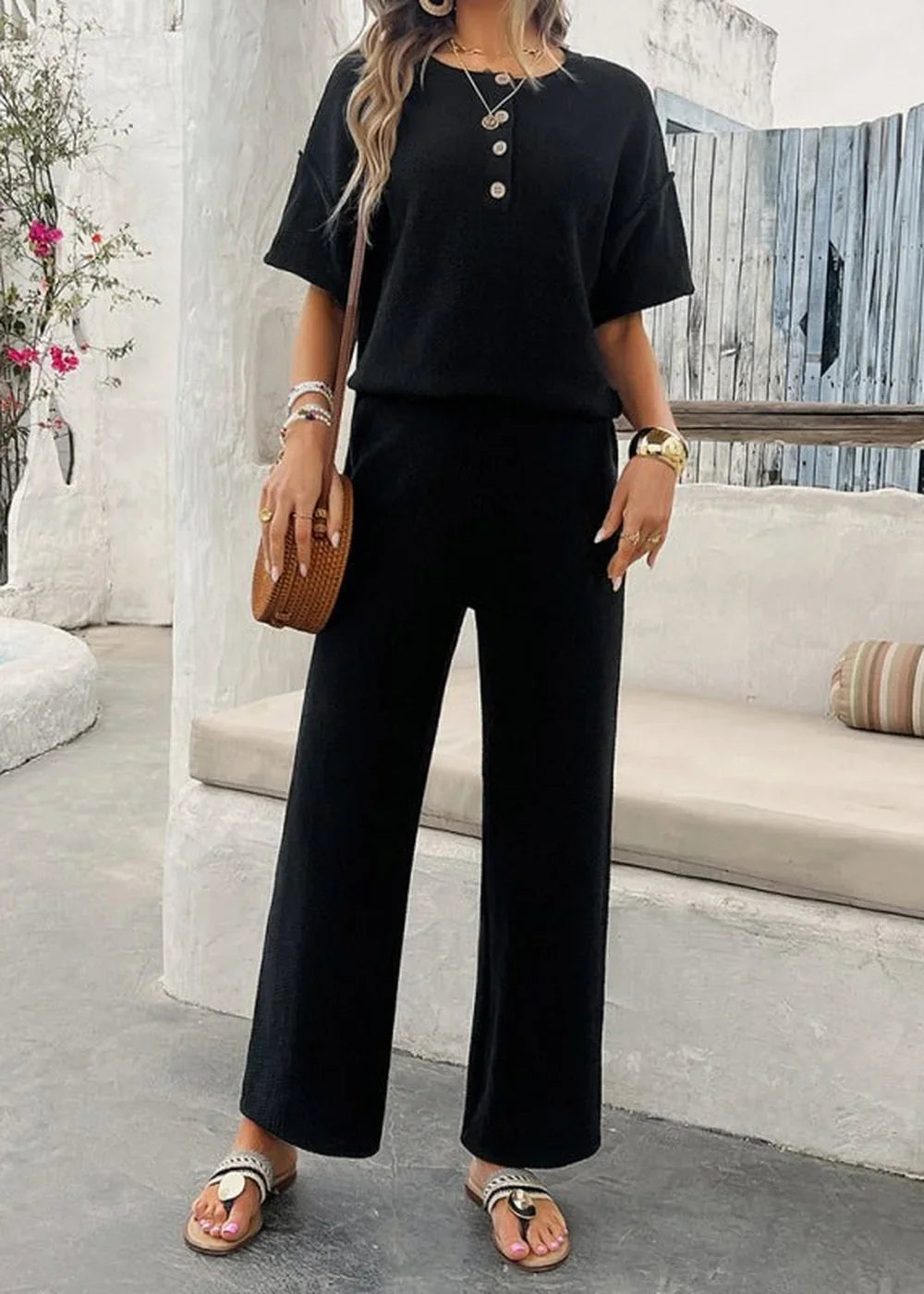 Model wears a black knit pant suit with short sleeves and wide-leg pants, paired with sandals.