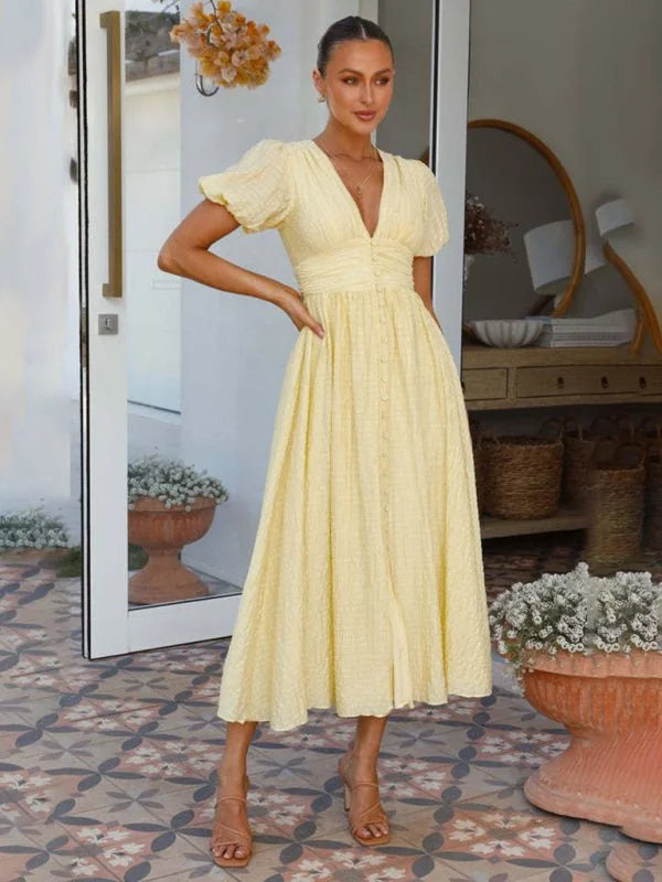 A woman in a yellow textured midi dress with puff sleeves and a V-neck, styled with tan heels.