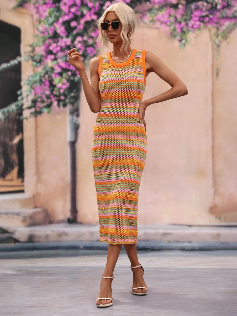 Woman in a striped knit midi dress with orange, pink, and green bands, paired with white sandals.