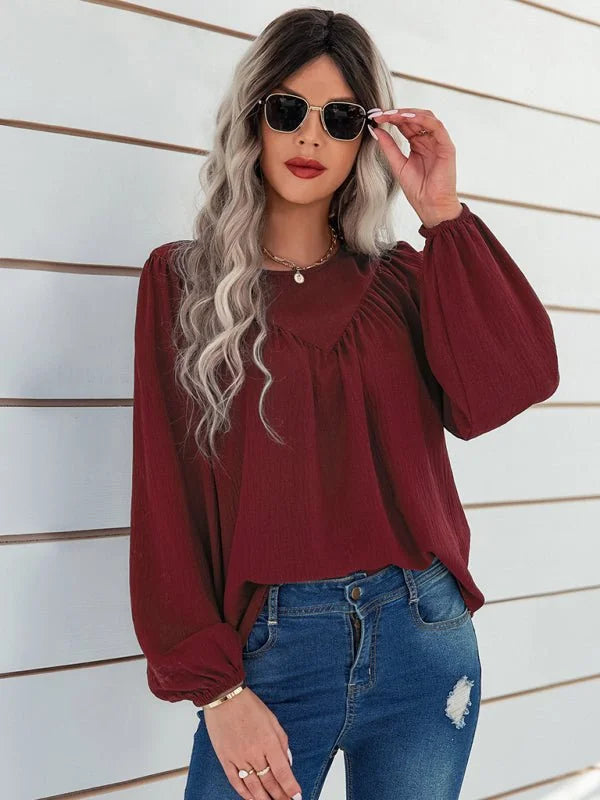Burgundy long-sleeve peasant top with textured fabric and blue distressed denim jeans on a model.
