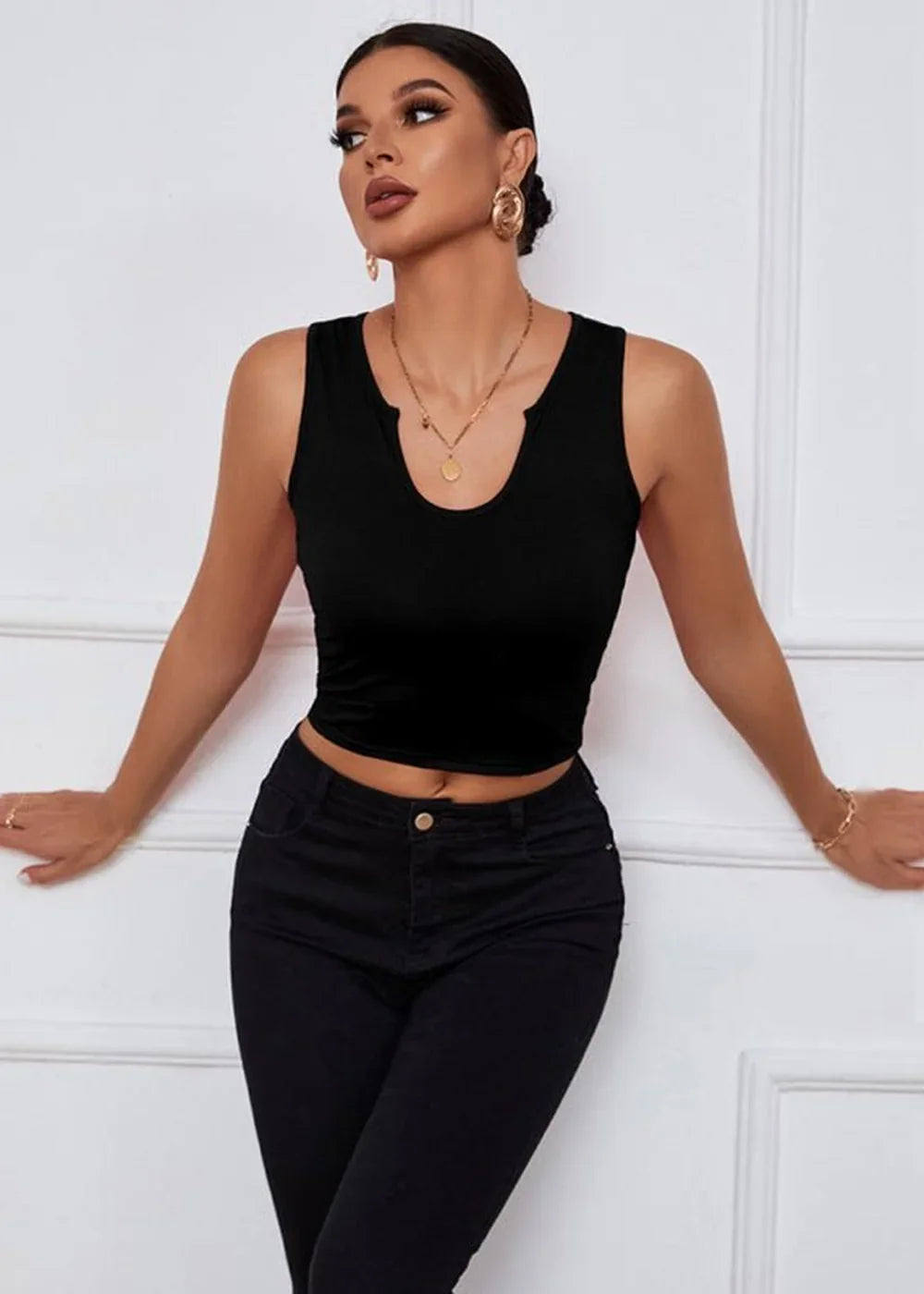 Black sleeveless crop top with a notch neckline and fitted black jeans on a model.
