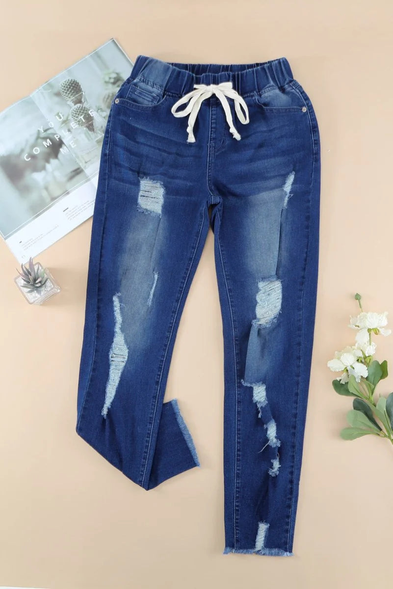 Distressed dark wash denim jeans with a drawstring waist and frayed hem.
