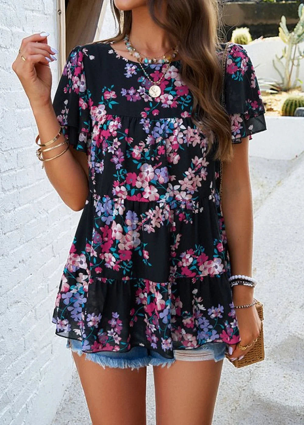 Black tiered chiffon top with a vibrant floral print and flutter sleeves, worn by a model.