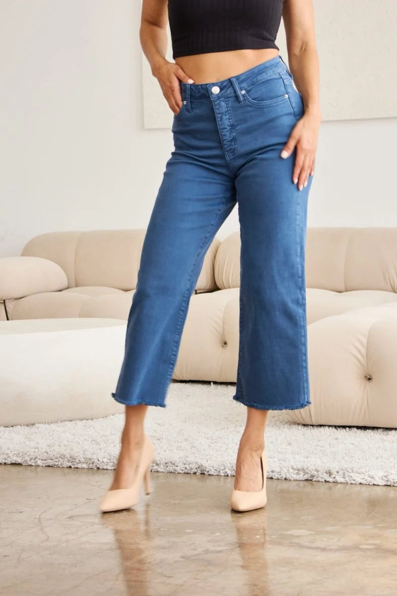 Blue cropped denim jeans with frayed hem, worn by a model on a couch.