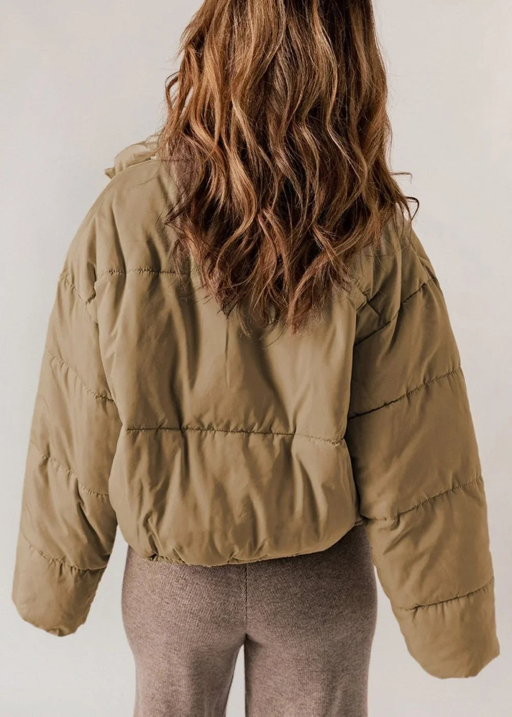 Back view of a woman wearing a cropped, khaki puffer jacket with textured, ribbed brown leggings.