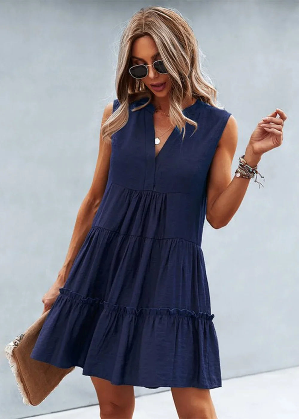 Navy blue tiered mini dress with V-neck, sleeveless, and ruffle hem, on a model.