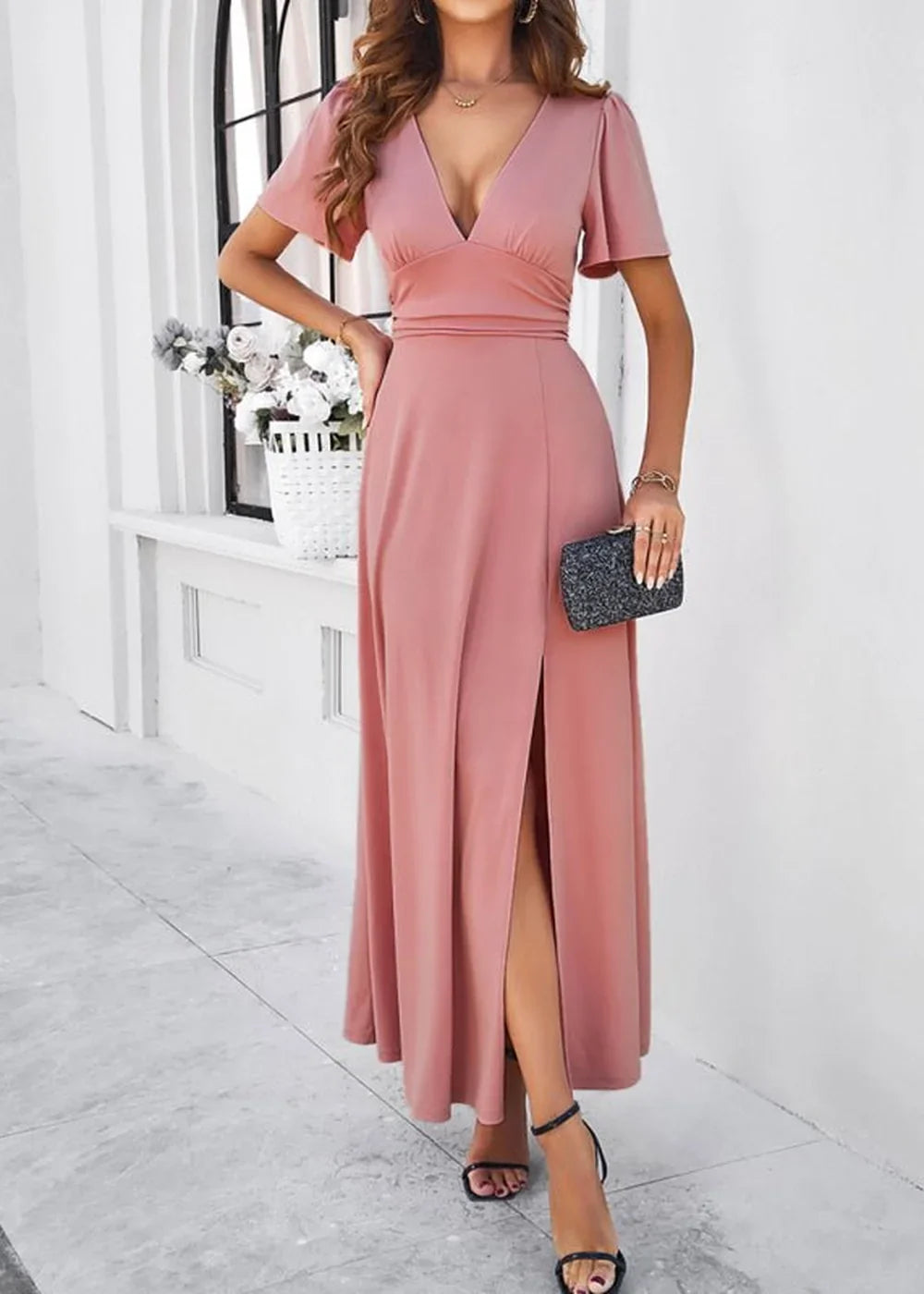 Pink flowy maxi dress with a deep V-neck and high slit, held by a model.