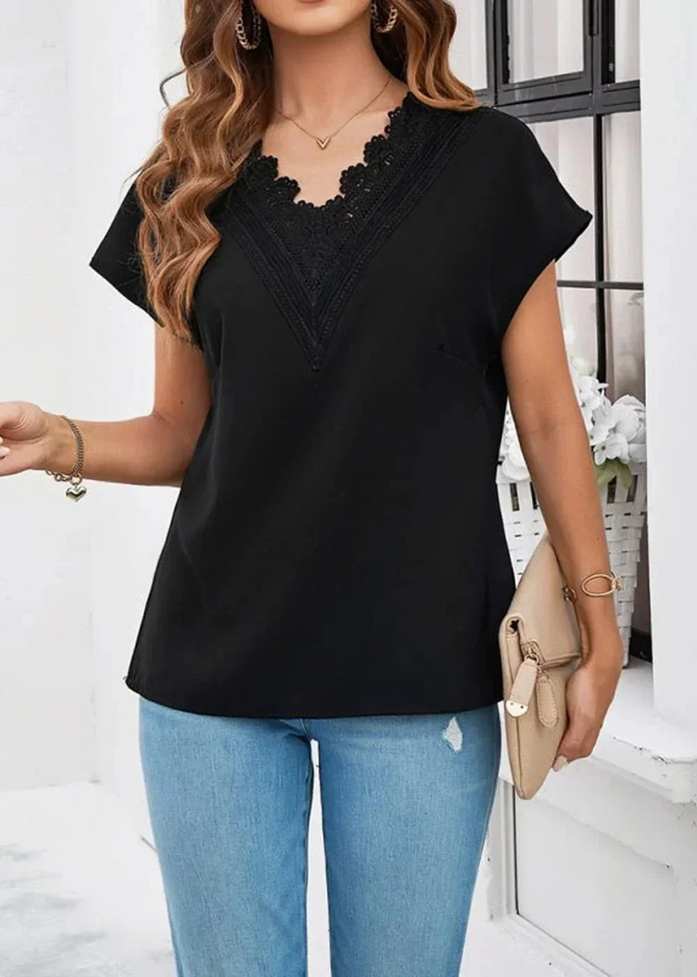 Black V-neck top with lace trim and short sleeves, worn by a model with light wash jeans and a beige clutch.