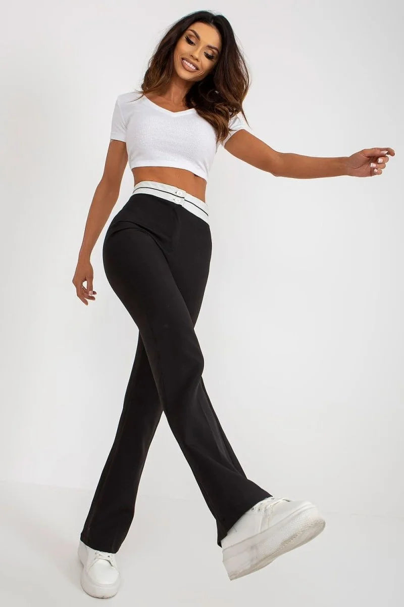 Black flared pants with a white waistband featuring two buttons, worn by a woman in a white crop top and platform sneakers.