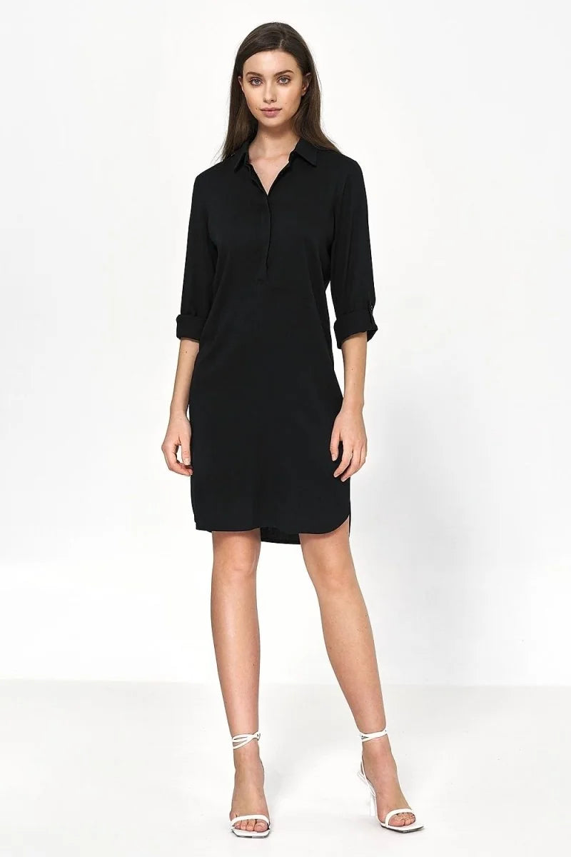 Full length black oversized viscose shirt dress with rolled sleeves and white strappy heels on model.