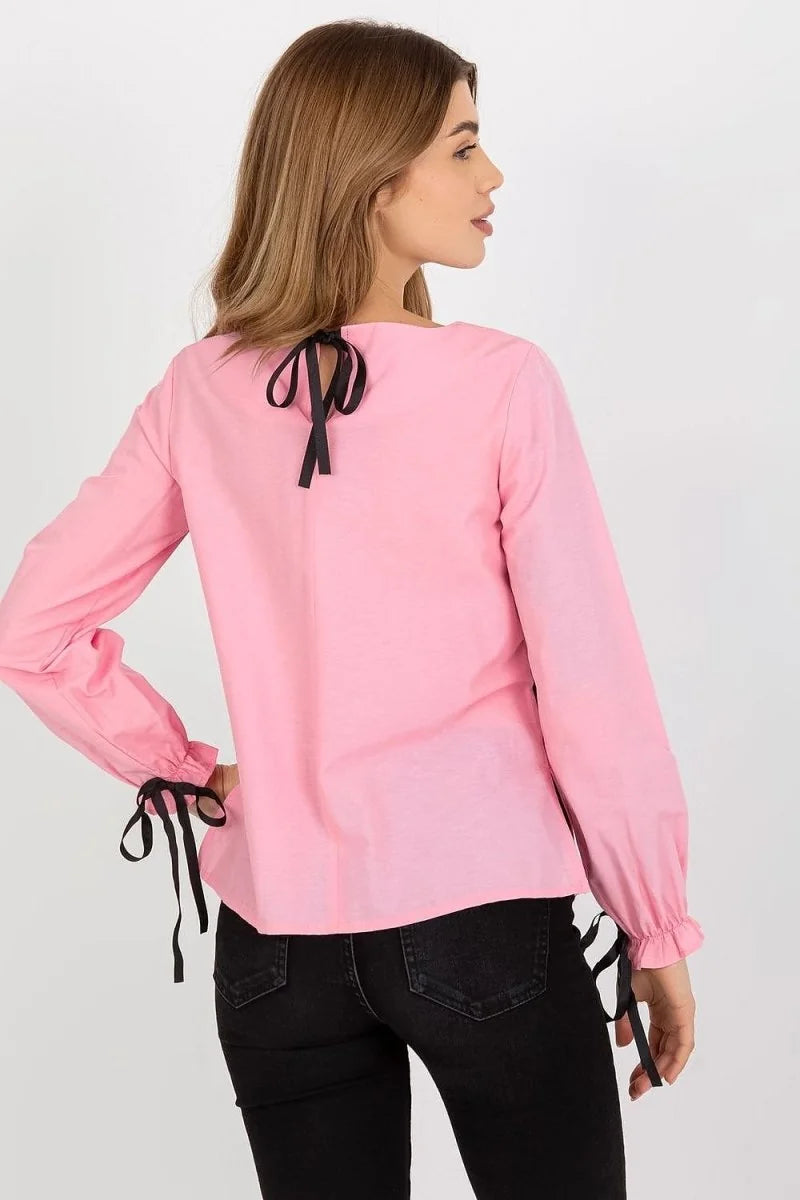 Woman in pink cotton blouse with black ribbon ties on sleeves and back, paired with black jeans.