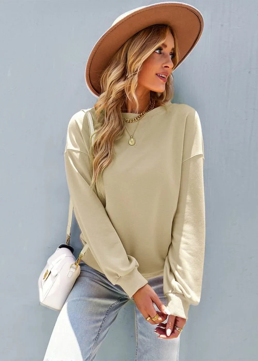 Woman in a loose-fit, light beige crewneck sweatshirt and light wash jeans, wearing a wide-brimmed hat.