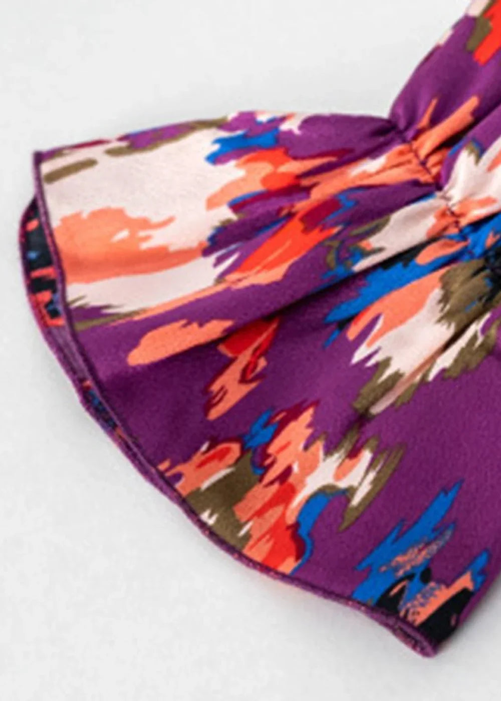 Close-up of a ruffled sleeve with a vibrant abstract floral print in purple, orange, pink, and blue.