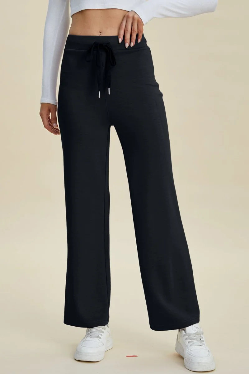 Black wide-leg pants with a drawstring waist and white sneakers on a model.
