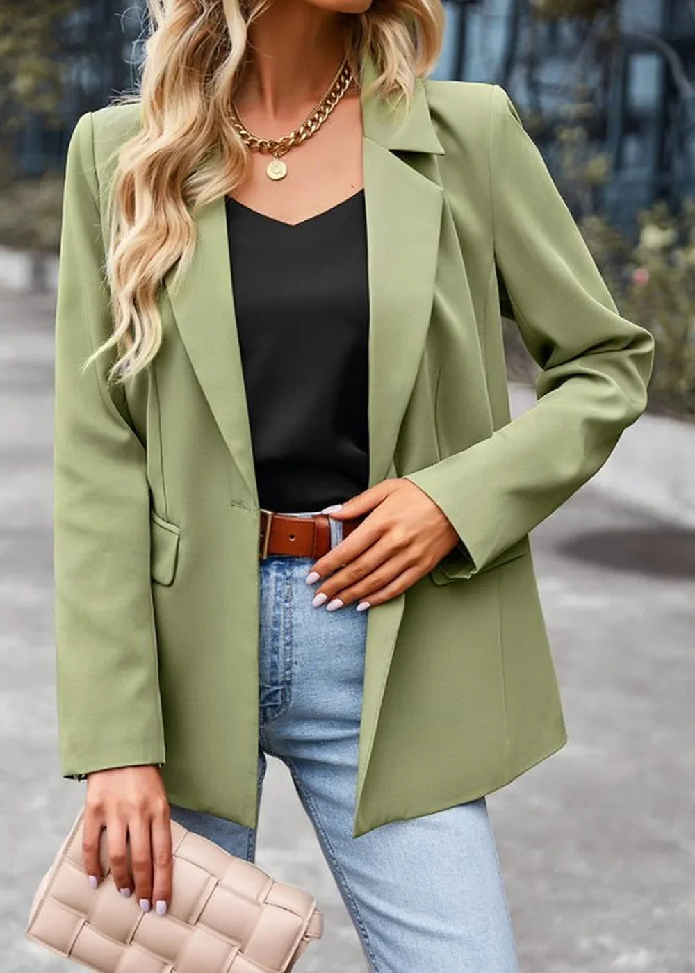 Woman in a light green blazer, black top, blue jeans, and a brown belt, holding a beige clutch.