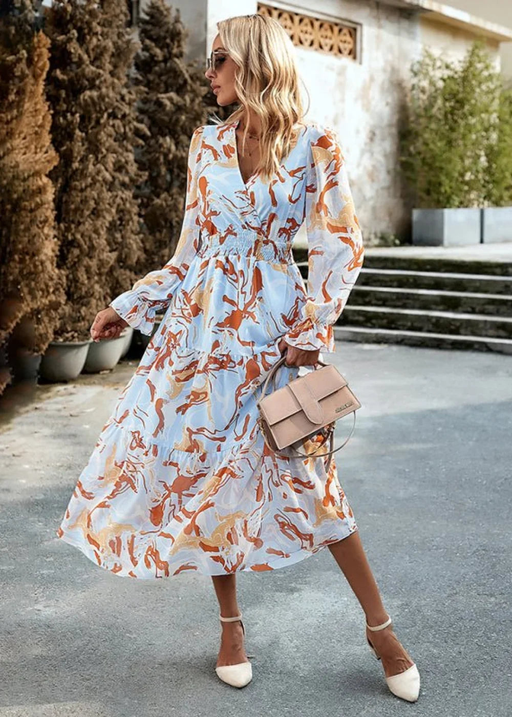 Light blue midi dress with orange abstract print, V-neck, long sleeves, and a nude crossbody bag.