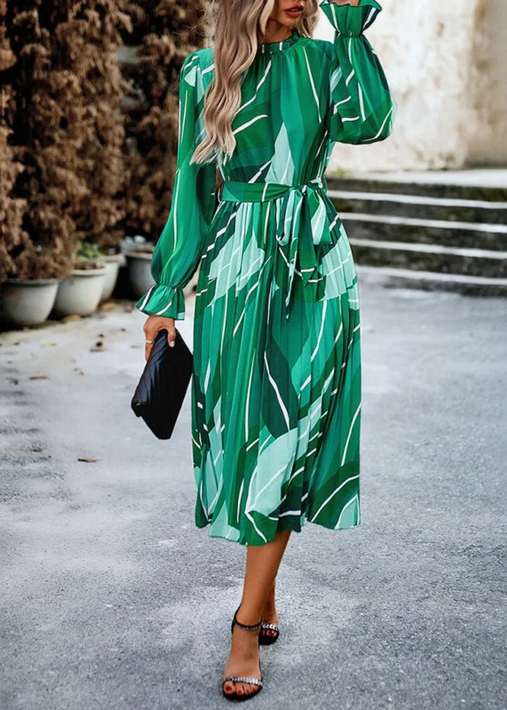 Woman in a green pleated midi dress with a white abstract print, cinched waist, and ruffled cuffs.