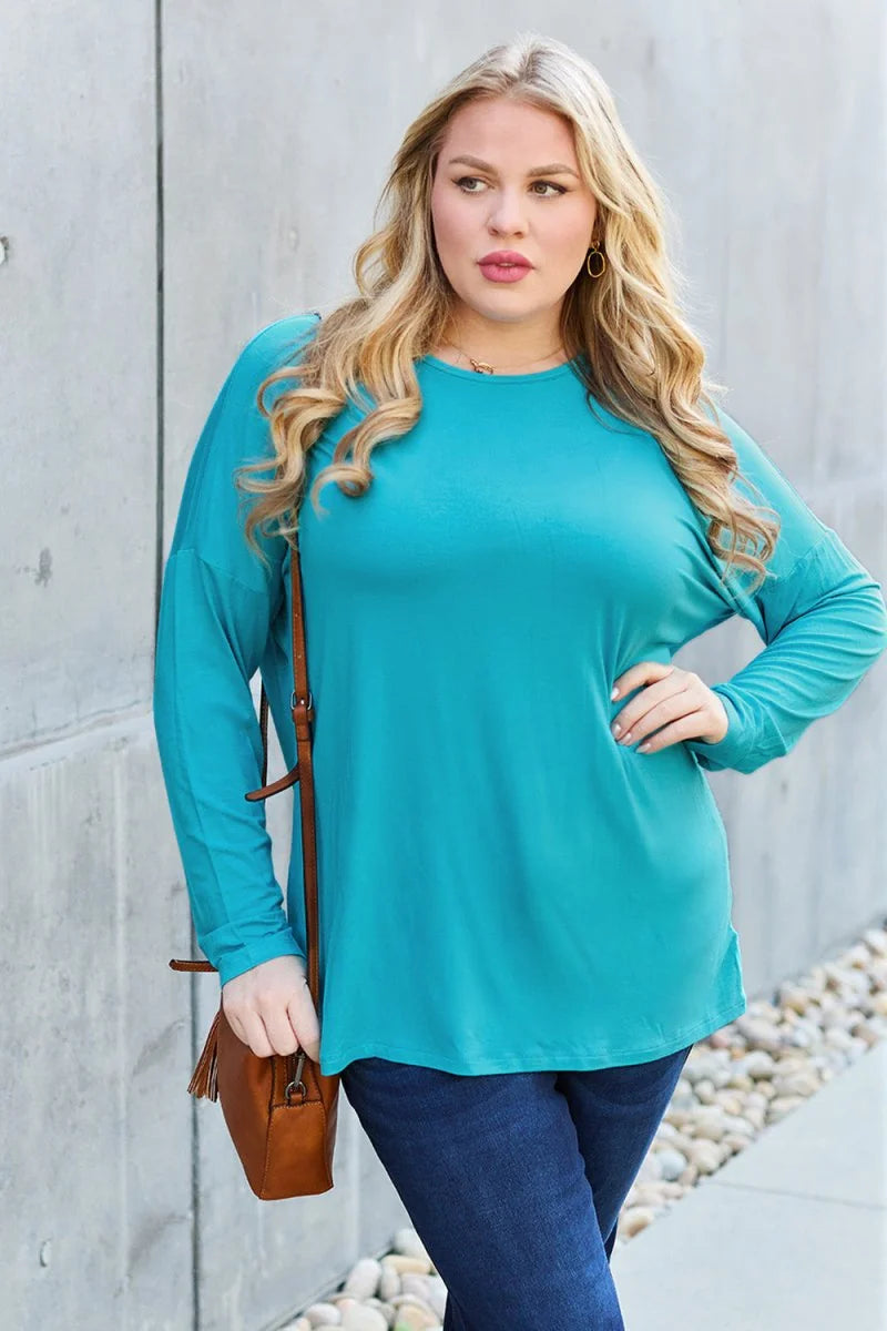 A woman in a teal long-sleeve top and dark wash jeans, with a brown crossbody purse.
